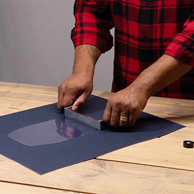 Une personne portant une chemise à carreaux rouge applique un adhésif sur une surface.
