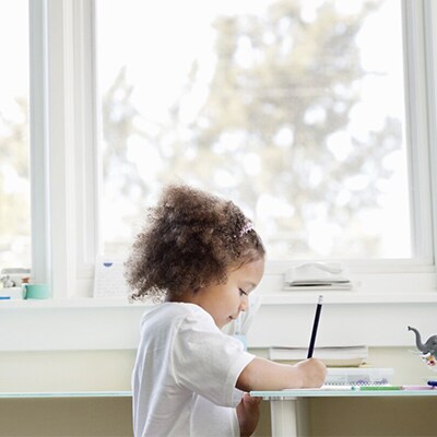 Un jeune enfant en train de dessiner devant une fenêtre.